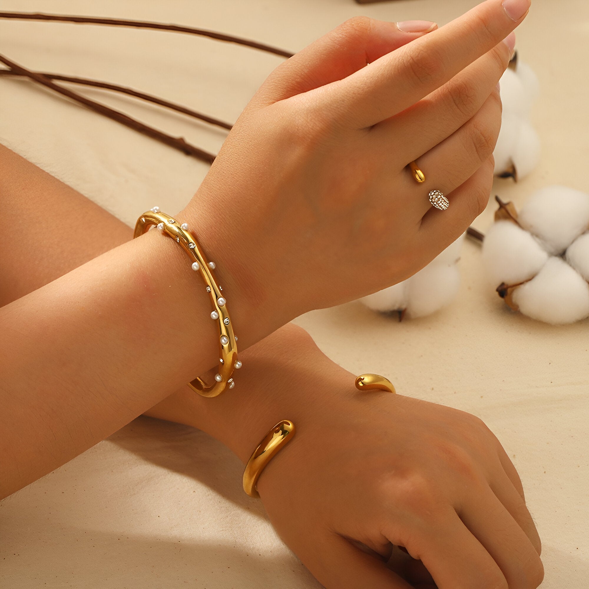 Bracelet jonc or fin orné de perles blanches délicates porté au poignet.