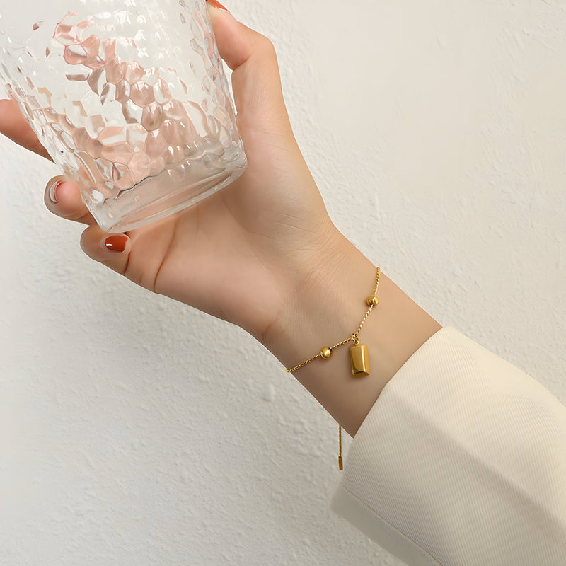 Bracelet jonc en titane plaqué or 18 carats à petit pendentif cylindrique, fin et élégant.