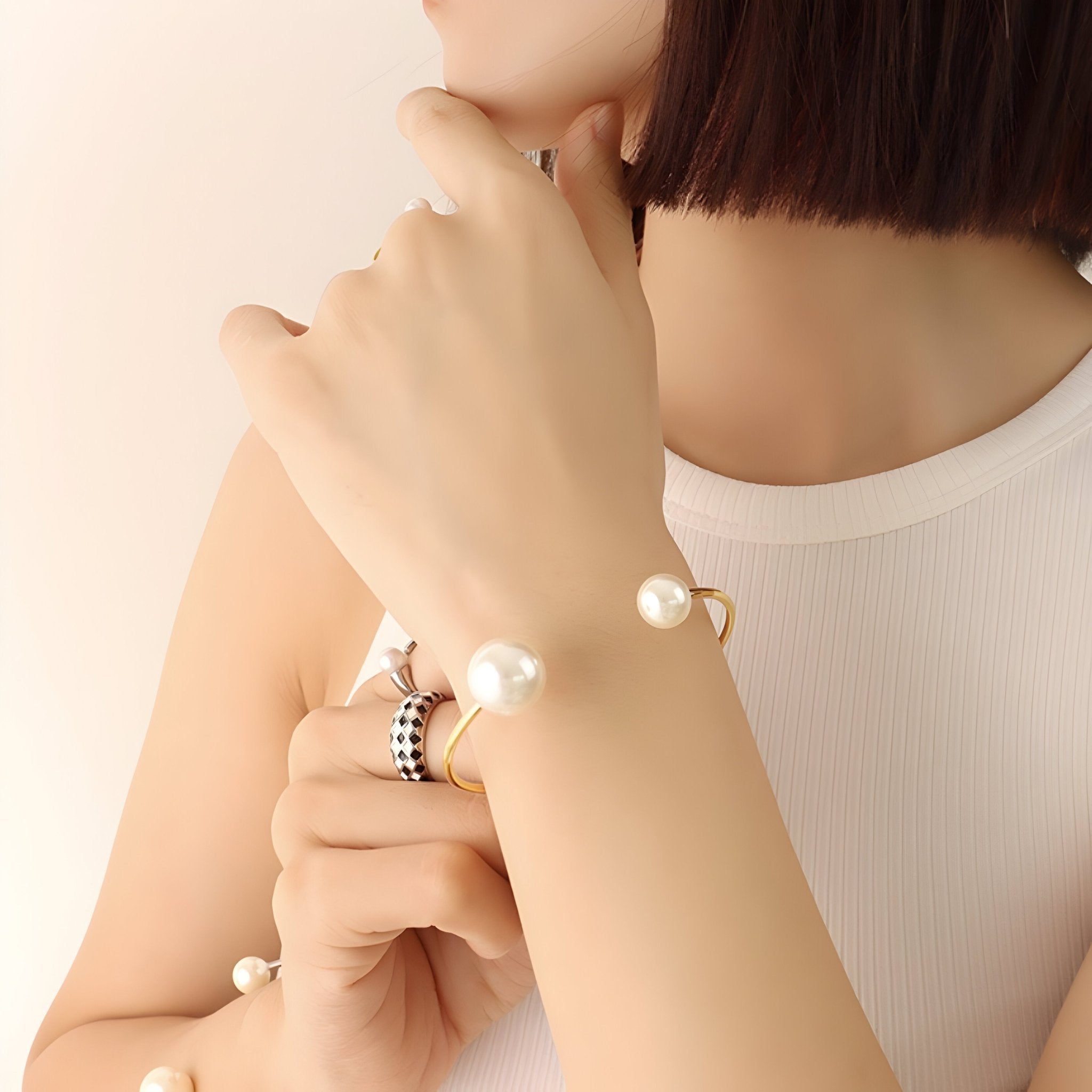 Bracelet jonc fin en titane plaqué or 18 carats avec perles d'imitation blanches aux extrémités, porté au poignet féminin.