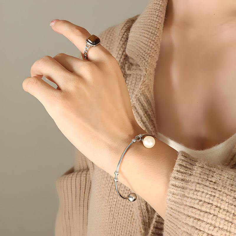 Bracelet jonc en titane plaqué or avec perle blanche ronde, style élégant et minimaliste.