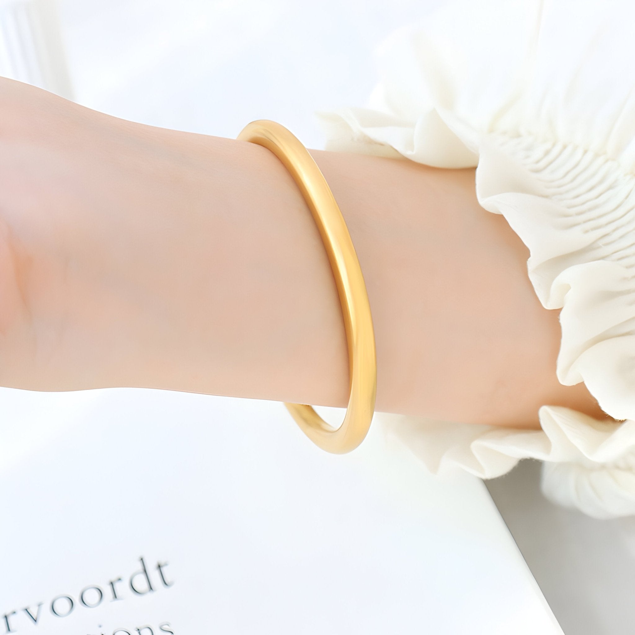 Bracelet jonc en titane plaqué or lisse et brillant porté au poignet féminin avec chemisier blanc à manche froncée.