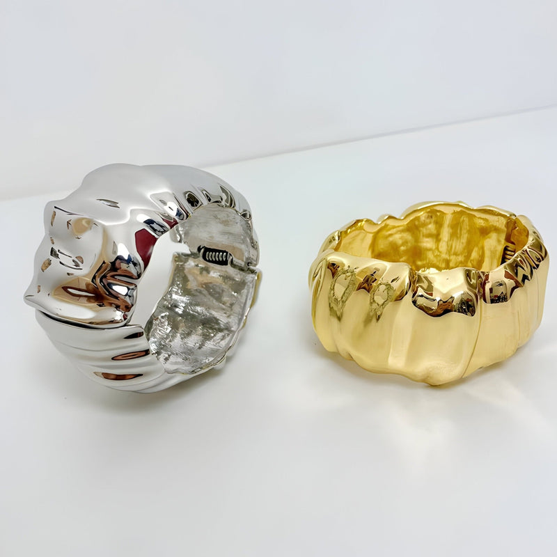 Bracelet manchette ondulé en métal argenté brillant et modèle or lisse aux reflets texturés.