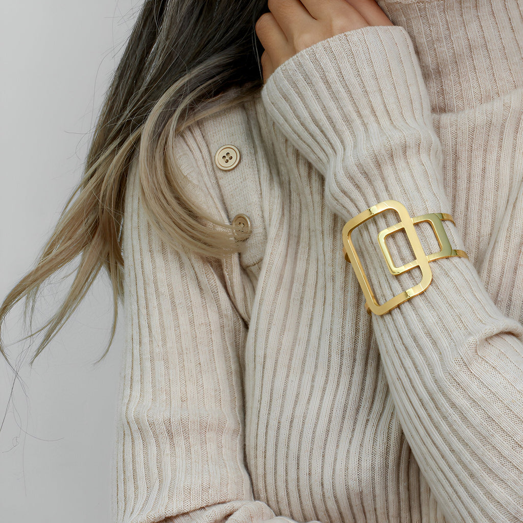 Bracelet manchette en métal doré au design géométrique élégant porté sur un pull côtelé beige.