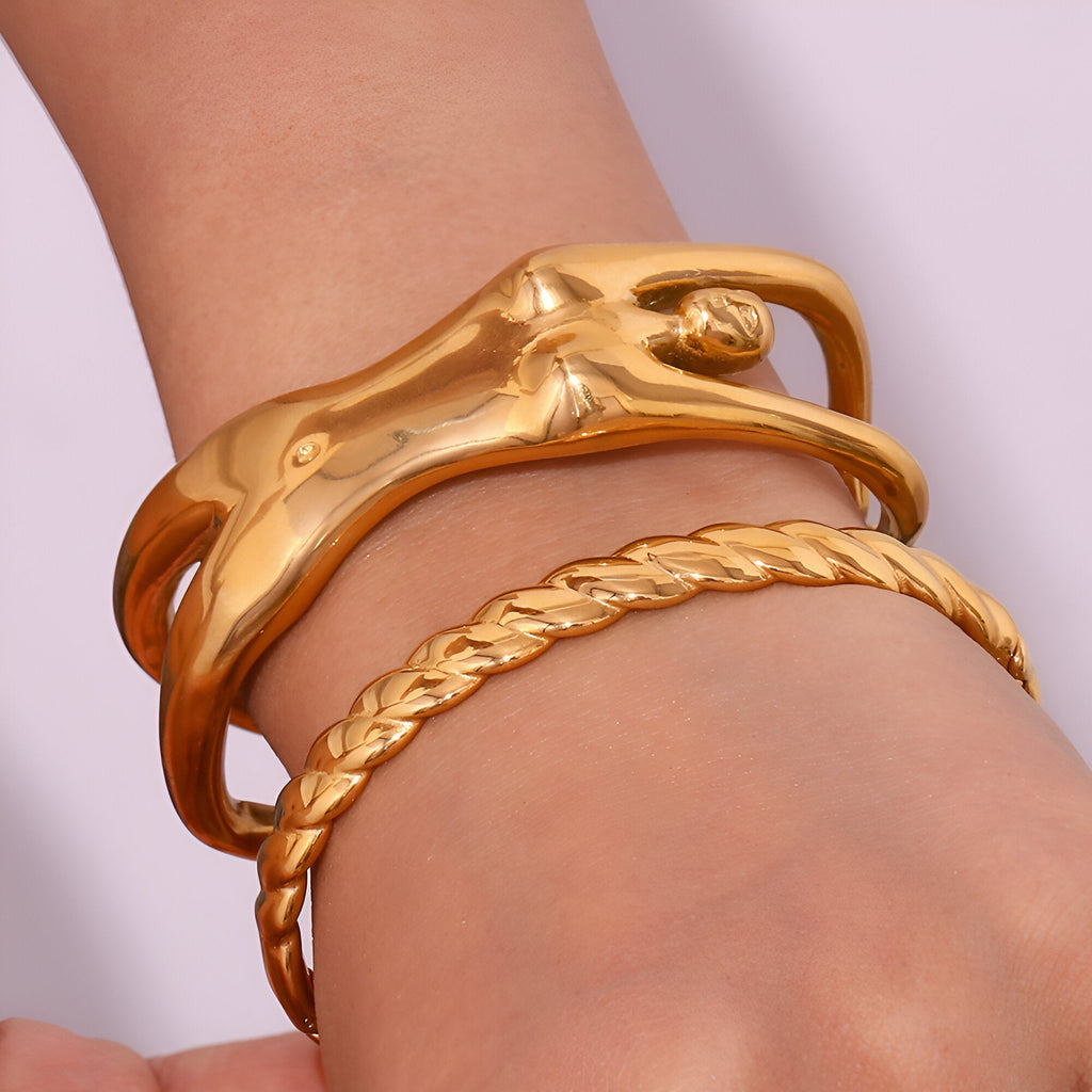 Bracelet manchette doré en forme de buste de femme avec surface lisse et poli, porté avec un bracelet torsadé or.