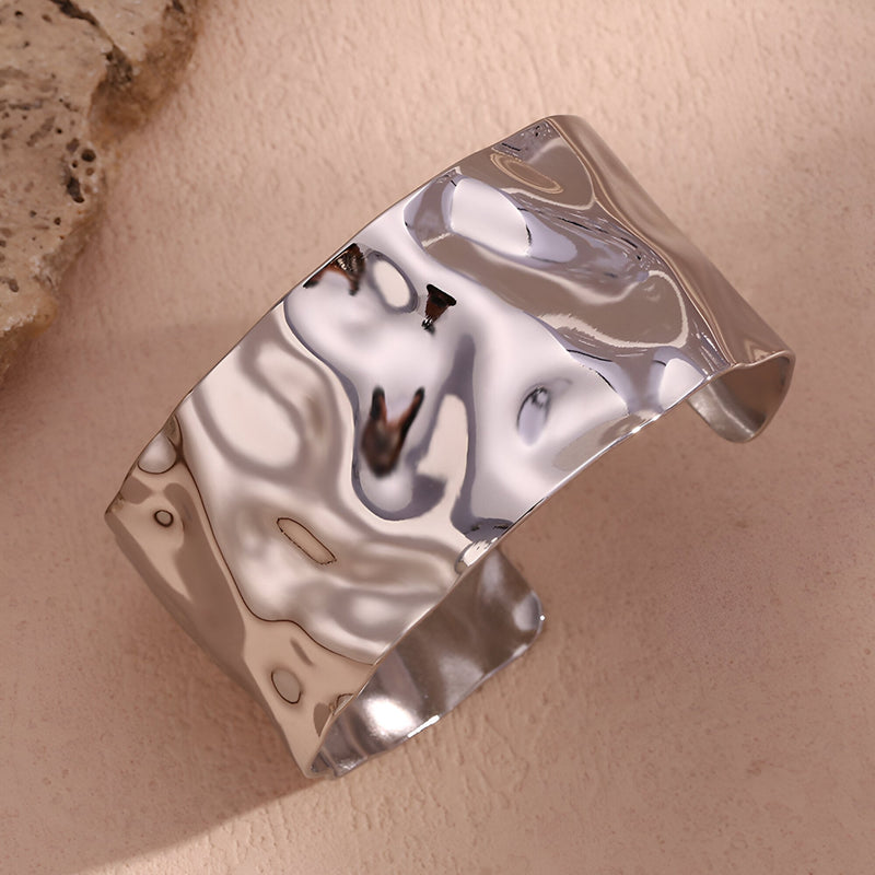 Bracelet manchette ondulé en acier inoxydable argenté brillant avec surface texturée fluide.