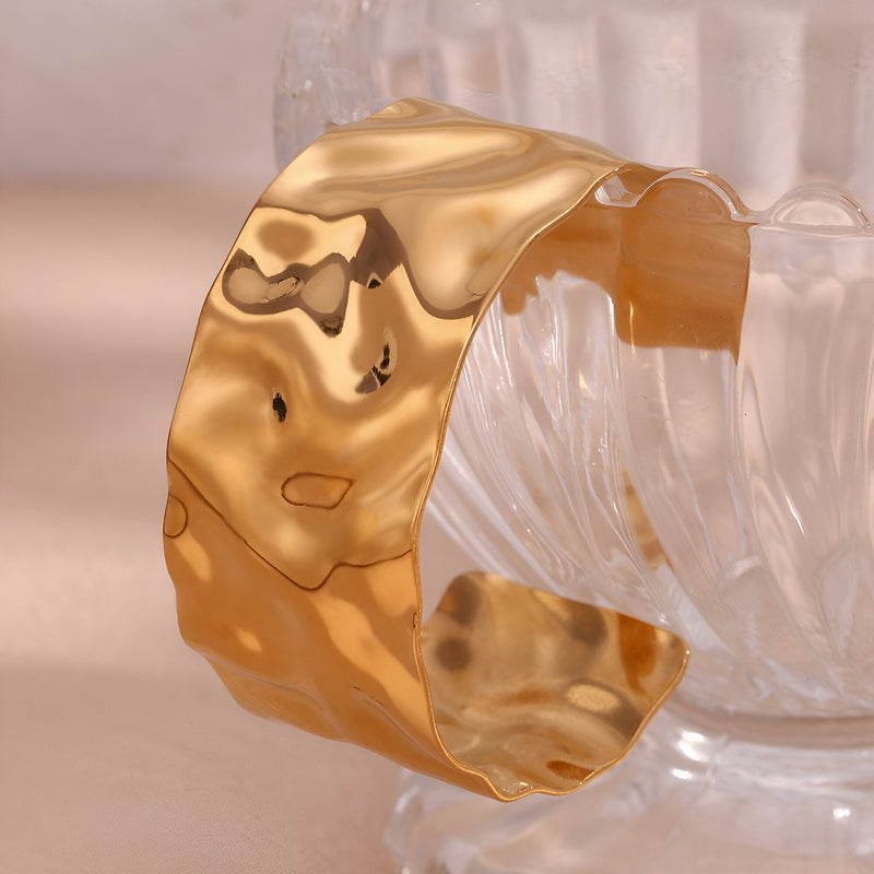 Bracelet manchette en acier inoxydable doré avec surface ondulée et finition brillante.