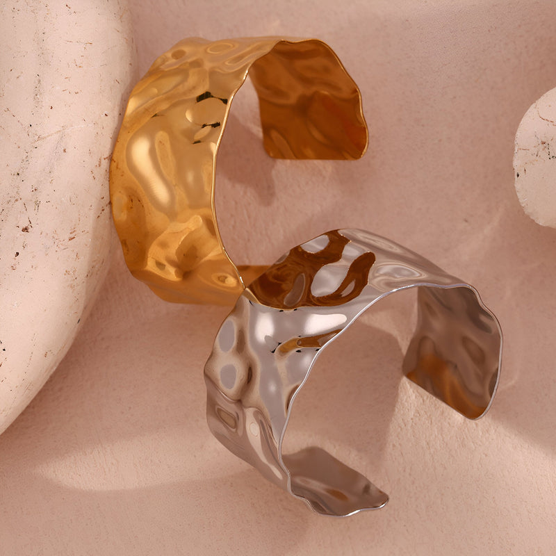 Bracelet manchette ondulé en acier inoxydable finition or brillant et argenté aux surfaces texturées et forme large.
