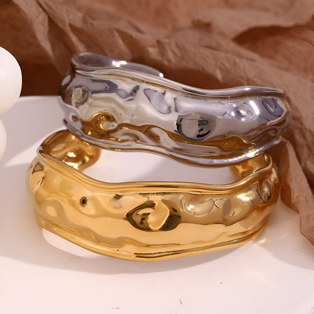 Bracelet manchette sculptural en acier inoxydable argenté brillant avec surface ondulée et reflet miroir.