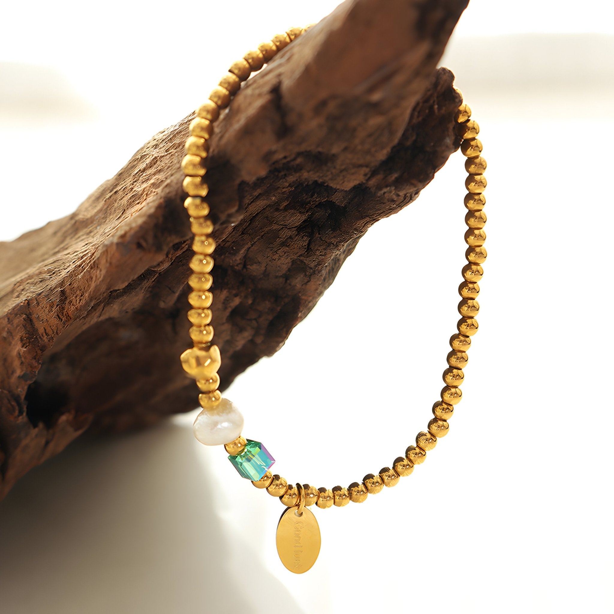 Bracelet perlé en titane doré avec perle d'eau douce, cristal bleu vert et médaille ovale dorée.