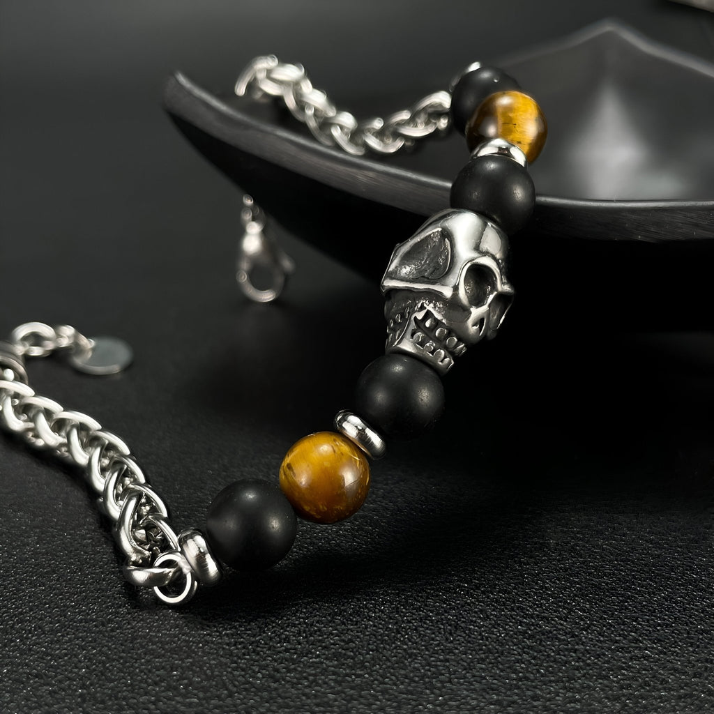 Bracelet homme en perles noires mat, perles œil de tigre marron et breloque tête de mort argentée sur chaîne acier.