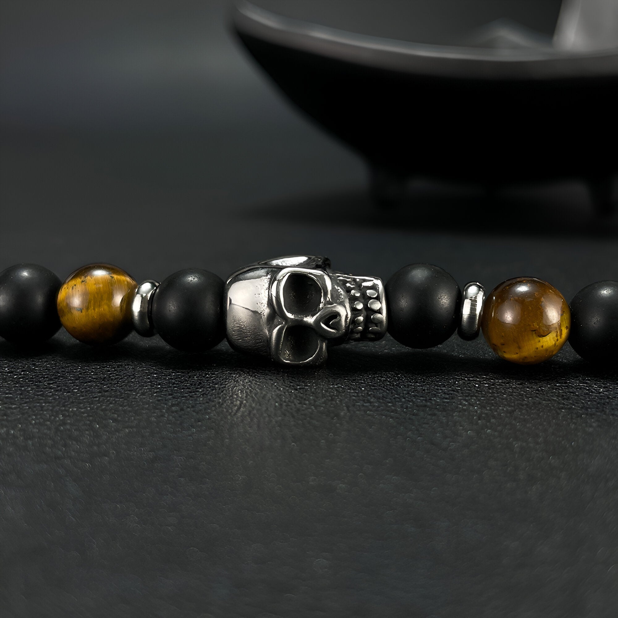 Bracelet homme avec perles noires, œil de tigre marron et tête de mort en métal argenté.