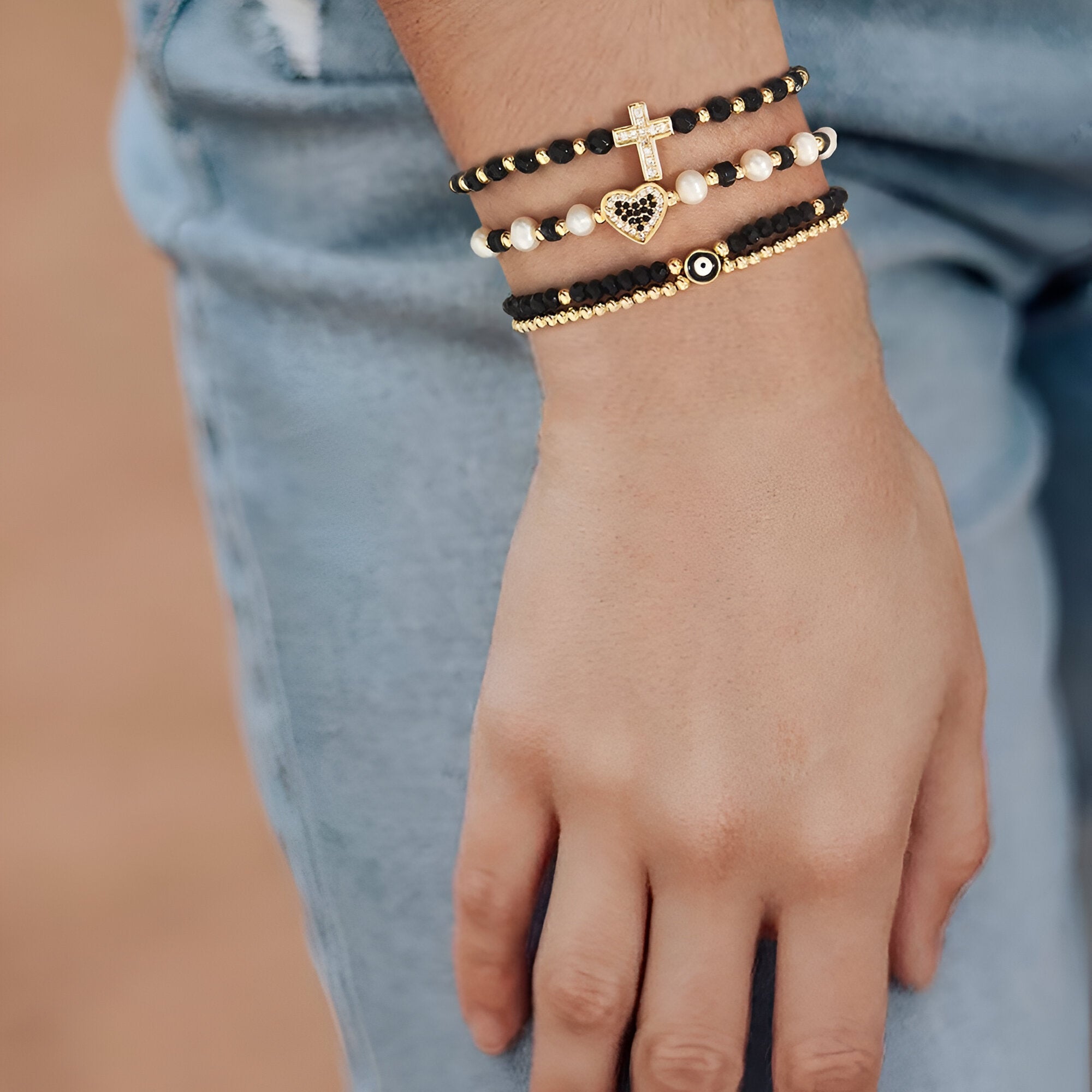 Trio de bracelets noirs à perles avec strass et breloques cœur et croix dorées.