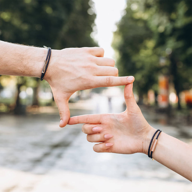 Bracelet cordon en cuir noir à enrouler, style fin et épuré, porté sur poignet masculin et féminin, outdoor flou en.