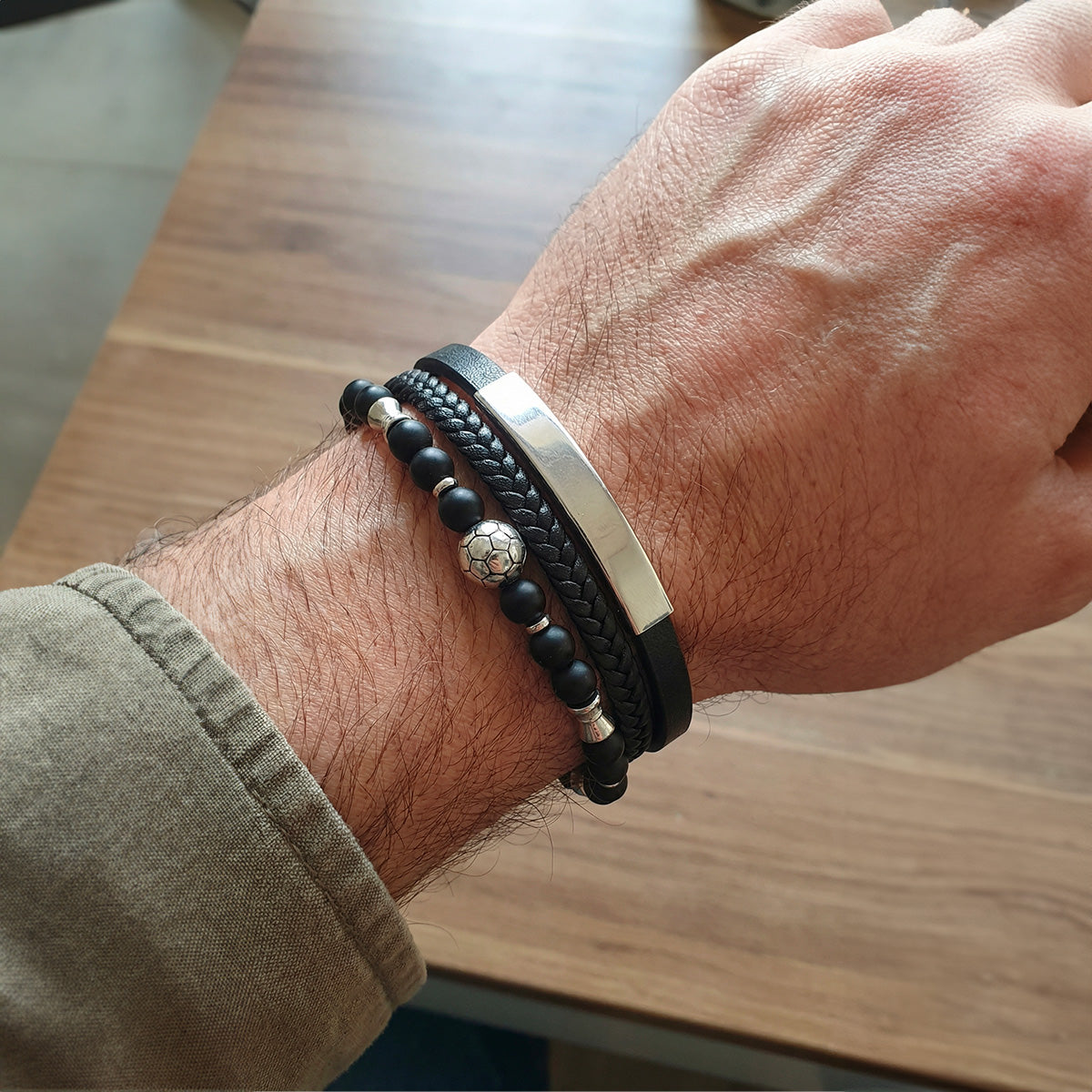 Bracelet masculin noir en cuir tressé avec perles noires et acier, fermoir magnétique, motif ballon de football argenté.