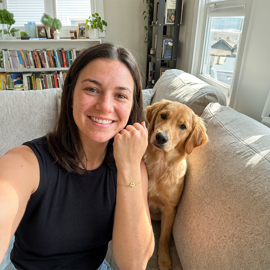 Bracelet en acier inoxydable doré avec pendentif en forme de patte, porté par une femme souriante sur un canapé gris.