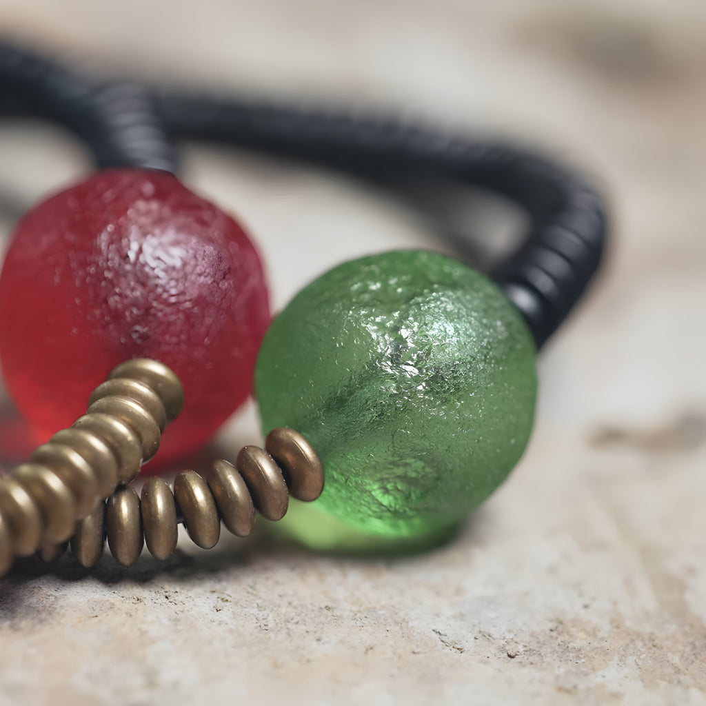 Bracelet en ébène noir avec perles en verre rouge et vert texturé, détails en métal cuivreux.