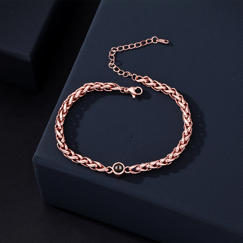 Bracelet maille tressée en acier inoxydable rose doré avec fermoir réglable et détail rond noir au centre.