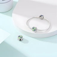 Charm trèfle à 4 feuilles argenté avec détails verts porté sur un bracelet argenté élégant.
