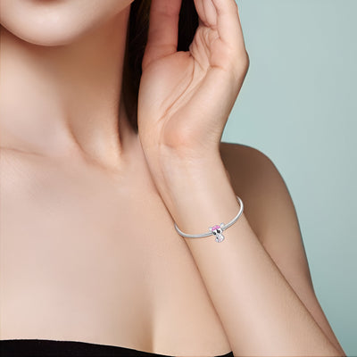 Bracelet argenté fin avec charm éléphanteau en métal et détail rose sur poignet féminin.