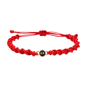 Bracelet tressé en nylon rouge avec fermoir coulissant et médaillon noir circulaire au centre.