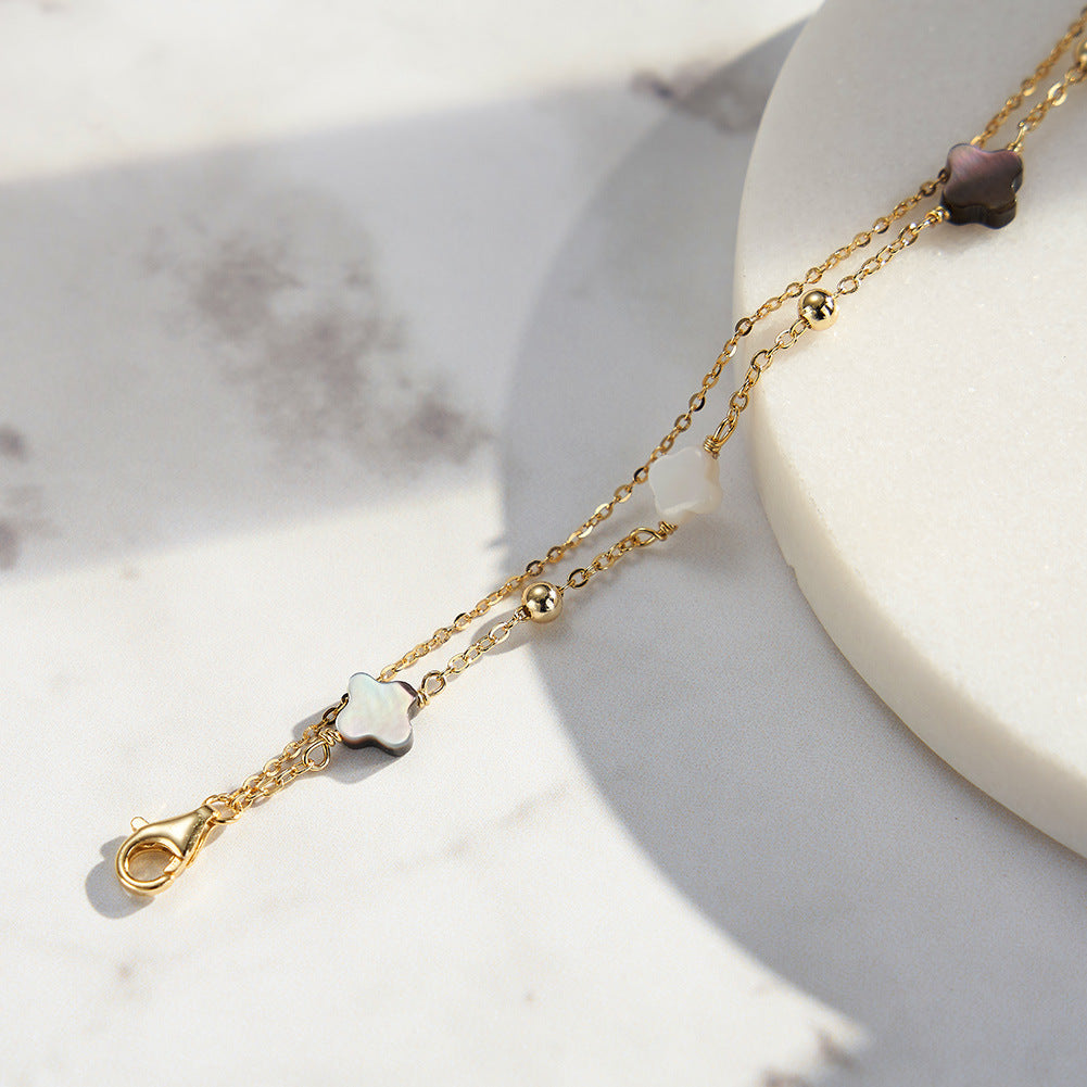 Bracelet double chaîne dorée avec deux trèfles en nacre blanche et noire, style délicat et raffiné.