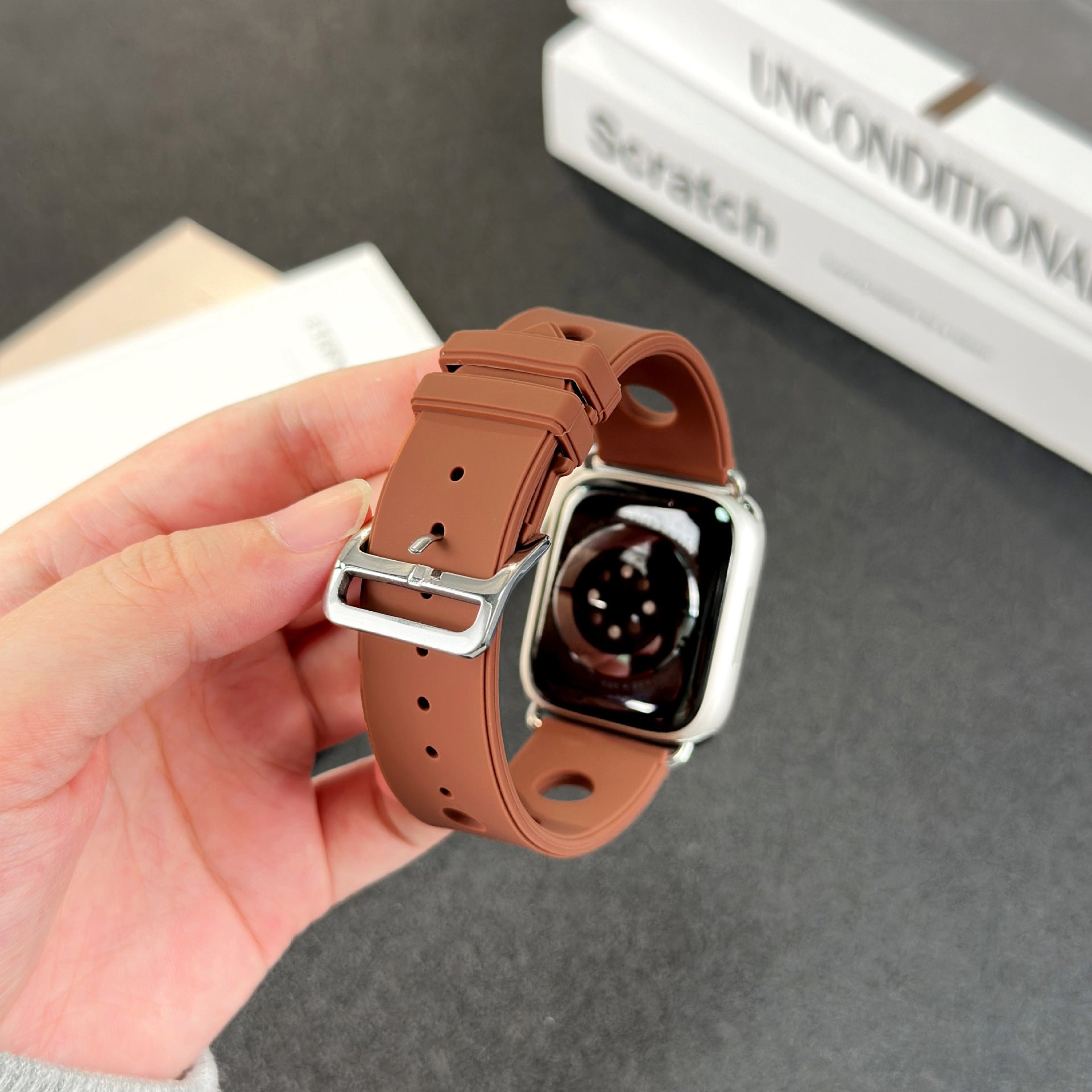 Bracelet Apple Watch en silicone marron perforé avec boucle ardillon en acier inoxydable, style sportif et respirant.