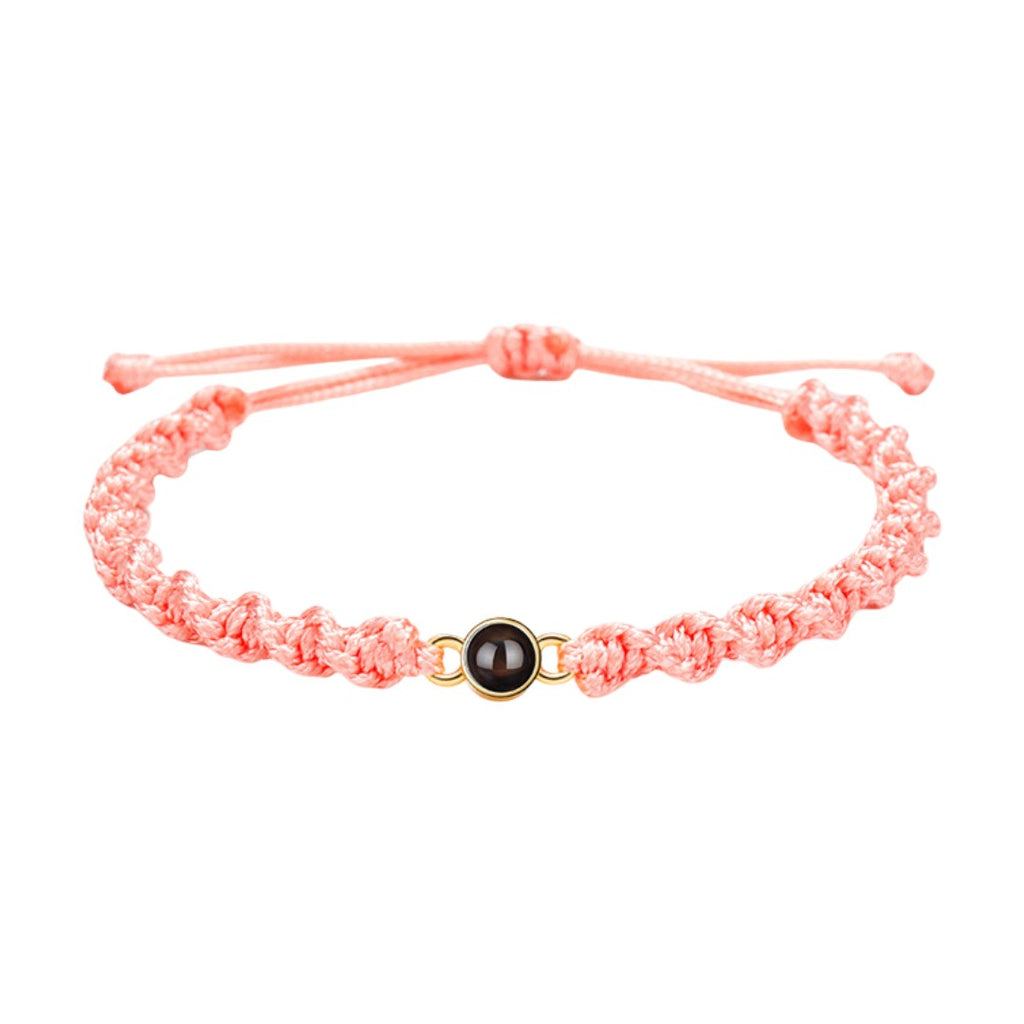 Bracelet tressé en nylon saumon avec fermoir coulissant et médaillon rond noir au centre.