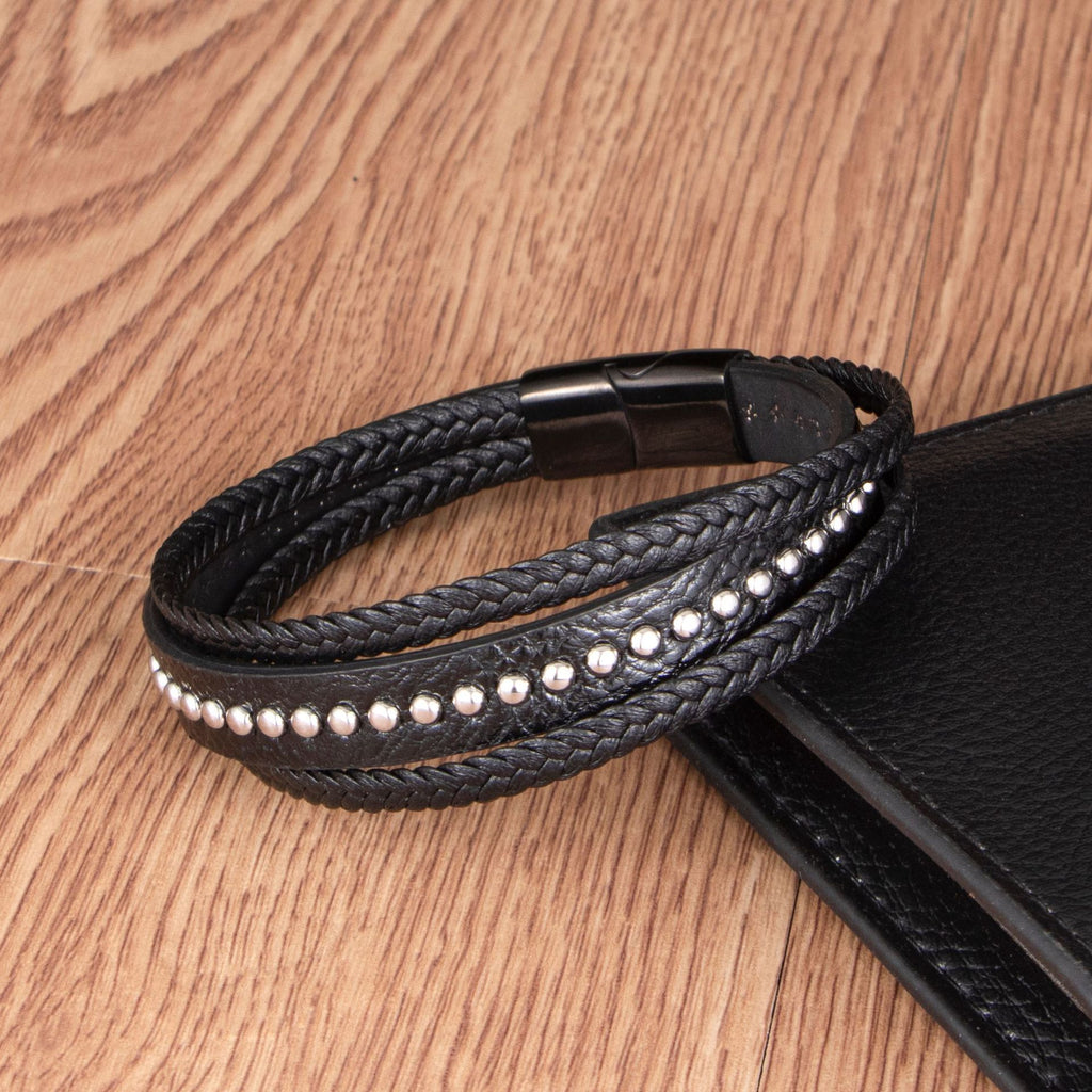 Bracelet multi-rangs noir en cuir tressé avec rivets métalliques et fermeture magnétique noire.
