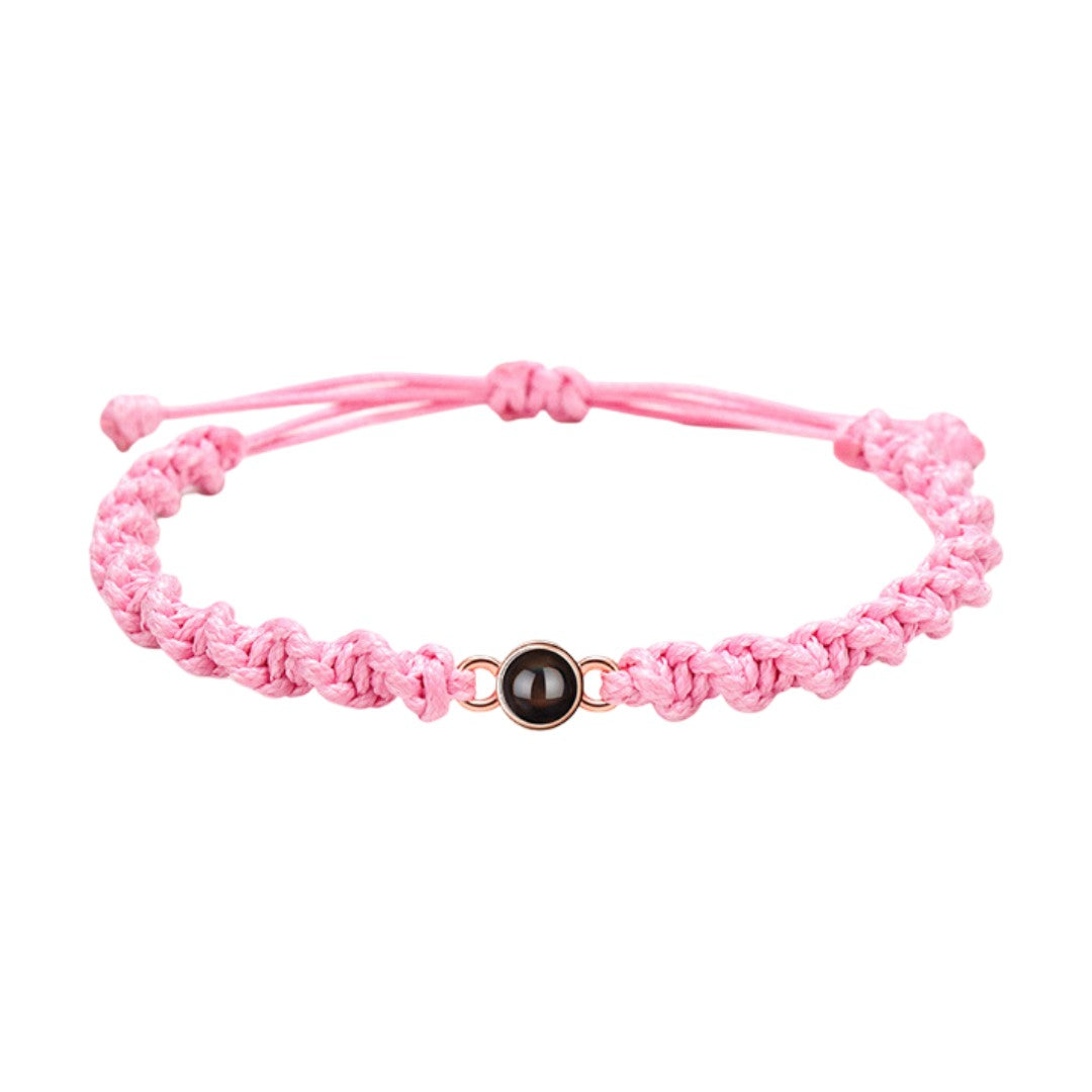 Bracelet tressé en nylon rose avec perle noire centrale et fermoir coulissant ajustable.