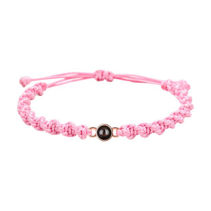 Bracelet tressé en nylon rose avec perle noire centrale et fermoir coulissant ajustable.