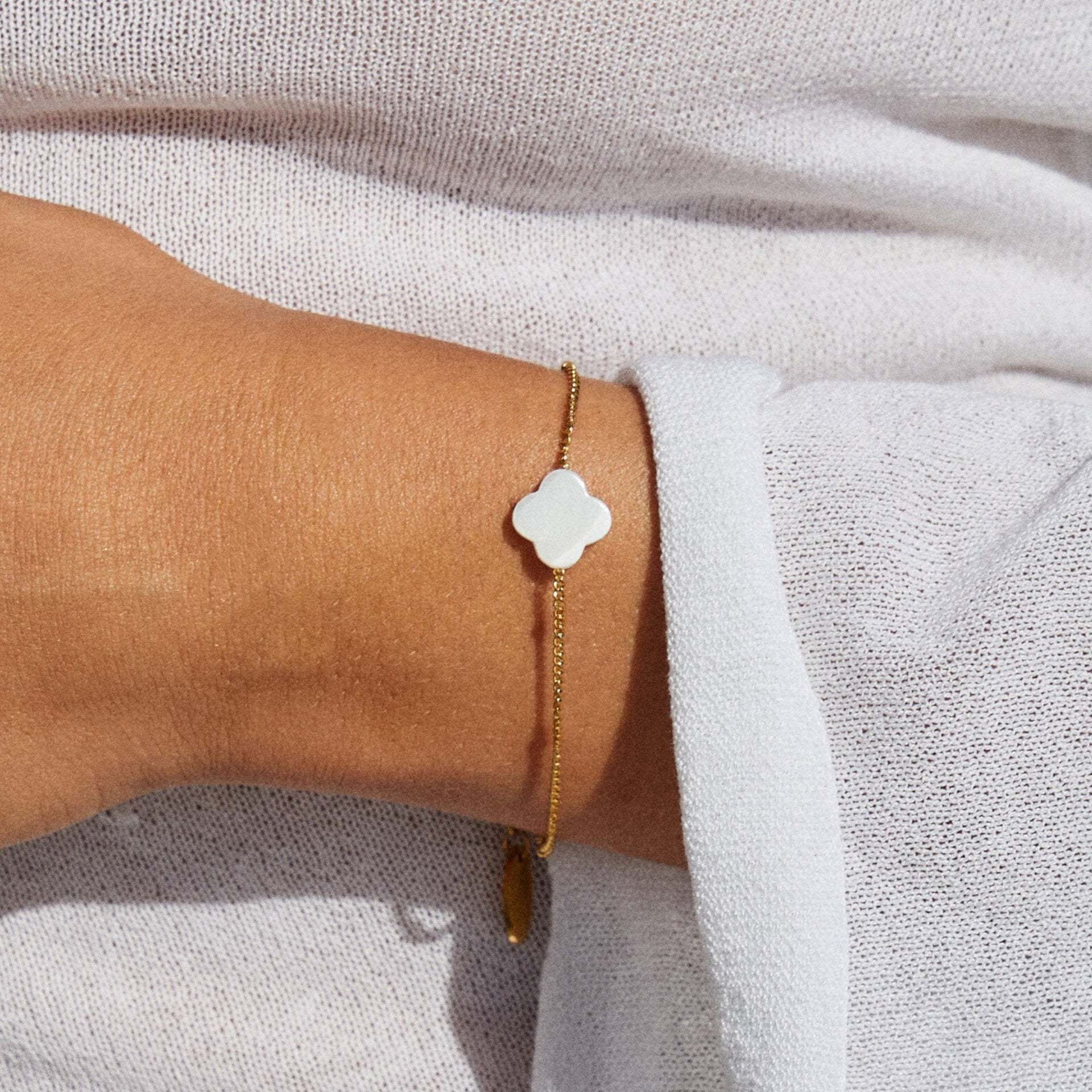 Bracelet fin doré avec chaîne délicate et pendentif trèfle en pierre naturelle blanche, ajustable.
