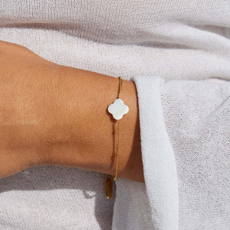 Bracelet fin doré avec chaîne délicate et pendentif trèfle en pierre naturelle blanche, ajustable.