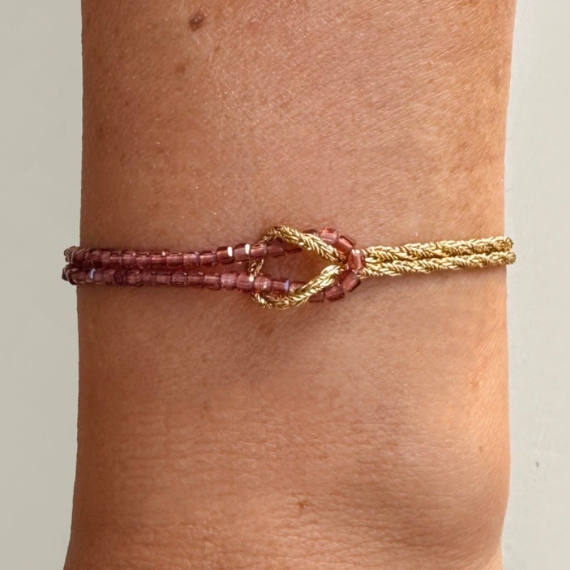 Bracelet double rang perles rouges et corde dorée torsadée avec fermoir mousqueton et nœud lumineux.