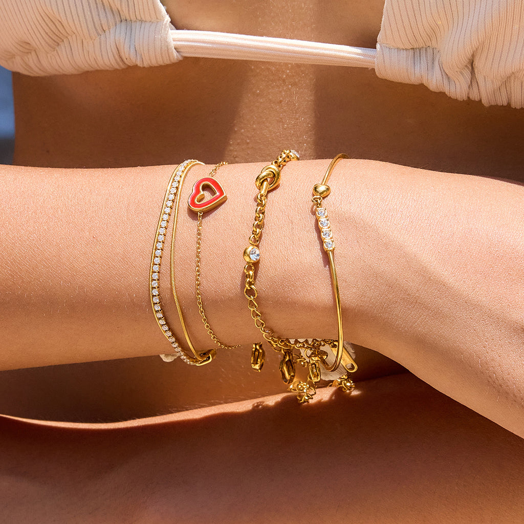 Bracelet jonc doré 18 carats avec cœur rouge et zircons scintillants, fermoir mousqueton, ajustable, porté au poignet.