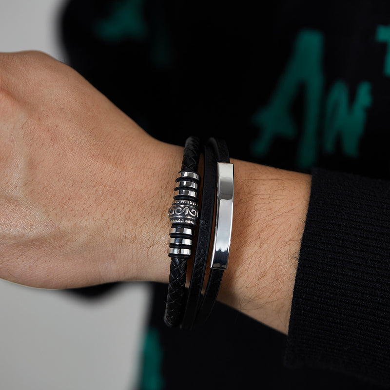 Bracelet homme en simili cuir noir avec plaques métalliques gravées et fermoir aimanté argenté, style moderne et élégant.