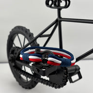 Bracelet cordon bleu blanc rouge avec mousqueton en acier inoxydable posé sur pédale de vélo noir miniature.
