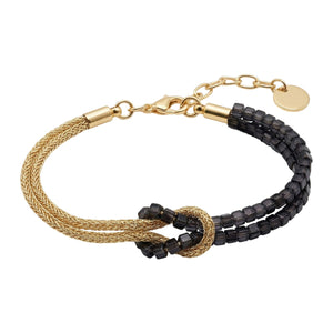 Bracelet double rang avec perles noires carrées et corde torsadée dorée, fermoir mousqueton et nœud décoratif lumineux.