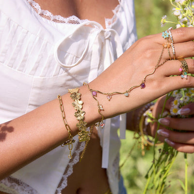 Bijou de main doré en acier inoxydable avec pierres naturelles colorées, chaîne fine ornée de détails floraux et pendentifs.
