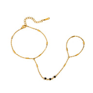 Bijou de main doré en acier avec chaîne fine, trois petits zircons noirs et anneau ajustable style bohème.