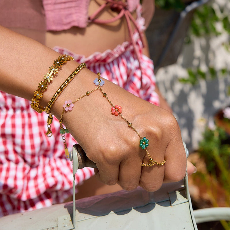 Bijou de main en acier inoxydable doré avec fleurs multicolores, chaîne fine reliant bracelet et bague, style romantique.