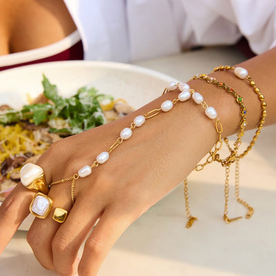 Bijou de main en acier inoxydable doré avec chaîne fine ornée de perles blanches, style chic et moderne.