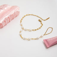 Bracelet de main en acier inoxydable doré avec perles blanches ovales et maillons fins rectangulaires.