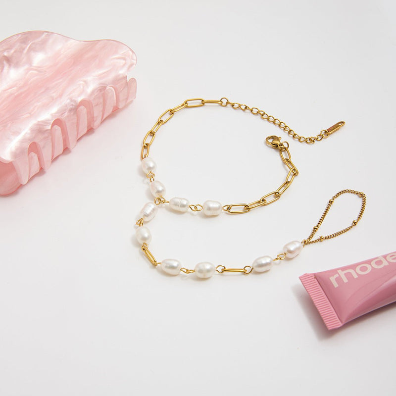 Bracelet de main en acier inoxydable doré avec perles blanches ovales et maillons fins rectangulaires.