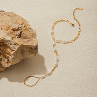 Bracelet de main en acier inoxydable doré avec perles blanches ovales et chaîne fine élégante.