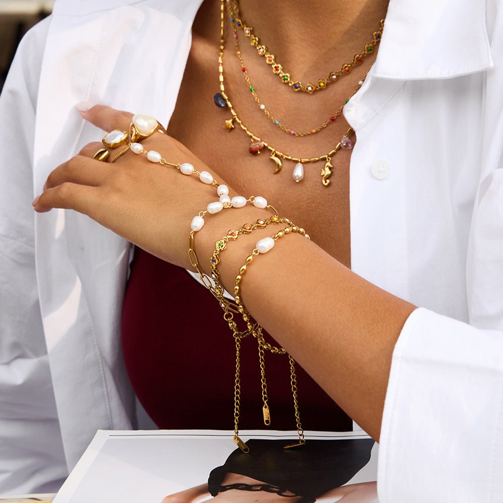 Bracelet de main en acier inoxydable doré avec perles blanches et chaînes fines, style chic et moderne.
