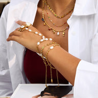 Bracelet de main en acier inoxydable doré avec perles blanches et chaînes fines, style chic et moderne.