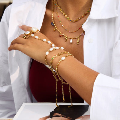 Bracelet de main en acier inoxydable doré avec perles blanches et chaînes fines, style chic et moderne.