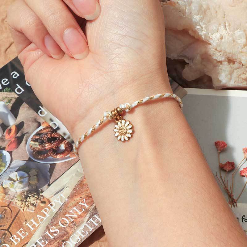 Bracelet fin en coton beige avec pendentif fleur en acier inoxydable doré.