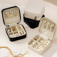 Boîte à bijoux nomade noire et blanche avec compartiments et montres en métal doré.