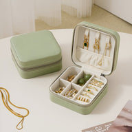 Boîte à bijoux nomade verte avec compartiments et crochets pour boucles d’oreilles, design compact et fermeture zippée.